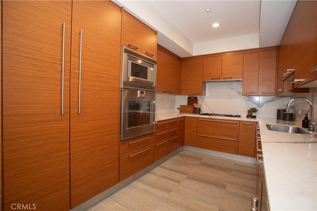 kitchen featuring tasteful backsplash, a sink, brown cabinetry, light countertops, and appliances with stainless steel finishes