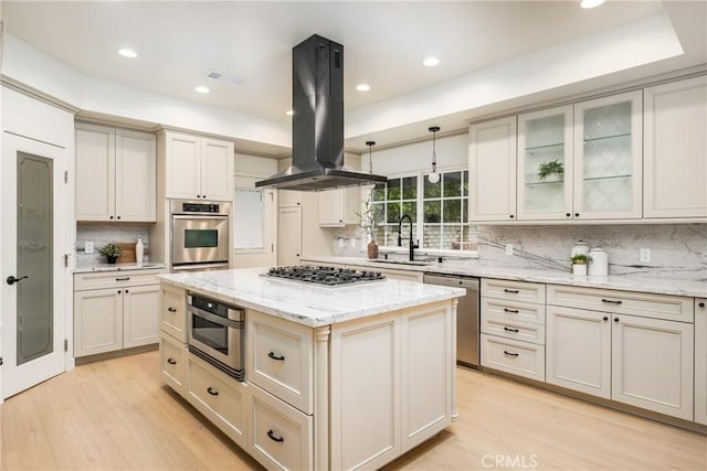 kitchen with sink, stainless steel appliances, island exhaust hood, light stone counters, and a kitchen island