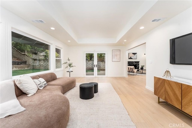 living room featuring french doors, a raised ceiling, and light hardwood / wood-style floors