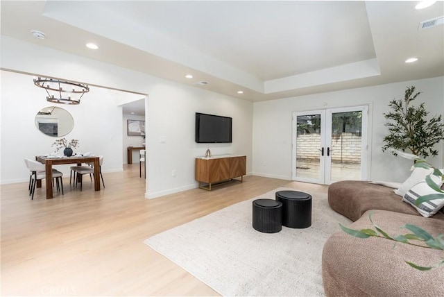 living room featuring a tray ceiling, wood-type flooring, and french doors