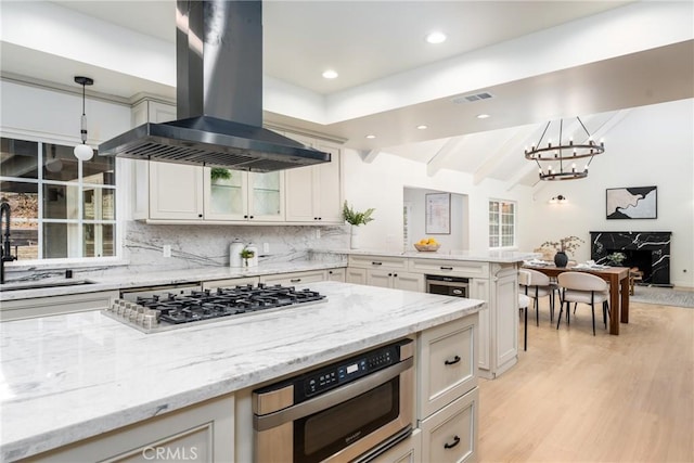 kitchen featuring sink, hanging light fixtures, light stone counters, island range hood, and stainless steel gas stovetop