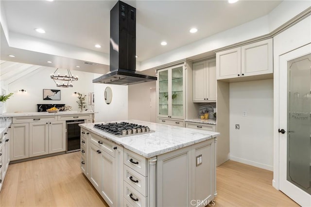 kitchen with a center island, light stone counters, stainless steel gas cooktop, island exhaust hood, and beverage cooler