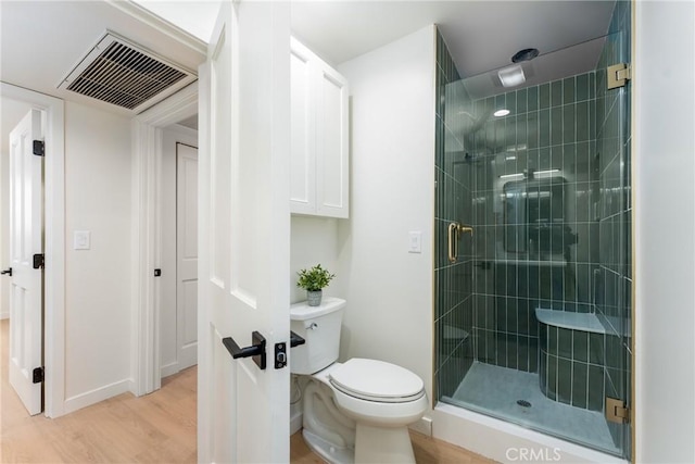 bathroom with hardwood / wood-style floors, a shower with shower door, and toilet