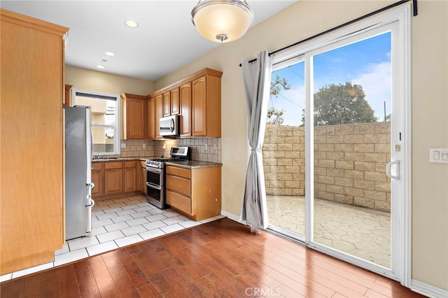 kitchen with tasteful backsplash, appliances with stainless steel finishes, plenty of natural light, and light wood-type flooring