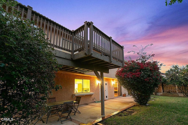 patio terrace at dusk featuring a balcony and a yard