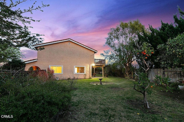 back house at dusk with a balcony and a lawn