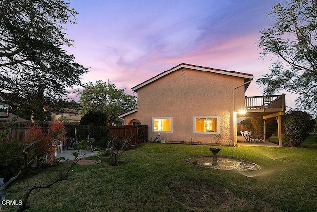 back house at dusk featuring a wooden deck, a yard, and a patio