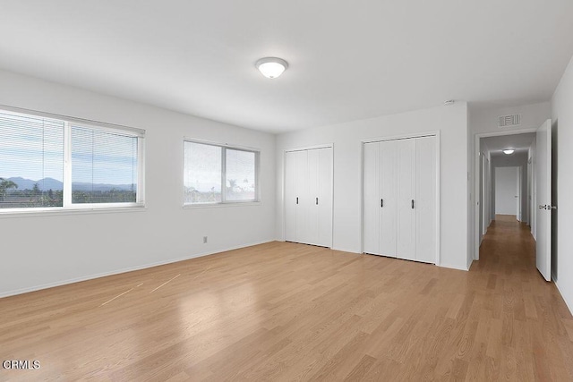 unfurnished bedroom with light hardwood / wood-style flooring and two closets