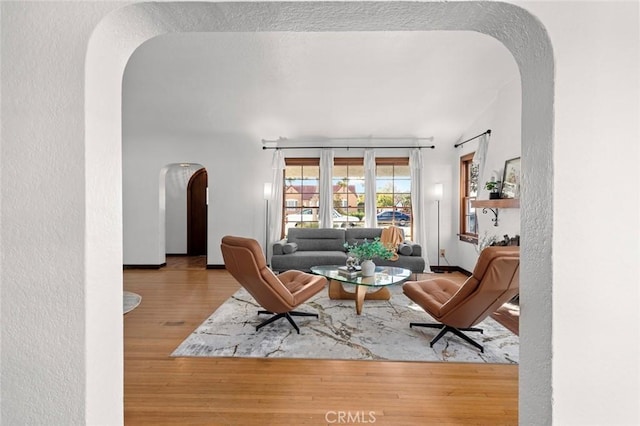 living area with arched walkways, a textured wall, and wood finished floors