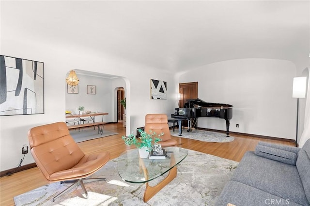 living area with arched walkways, lofted ceiling, baseboards, and wood finished floors