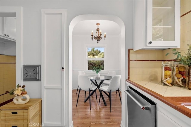 dining room with light wood-style floors, crown molding, arched walkways, and a notable chandelier