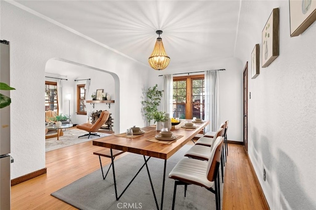 dining space featuring light wood-style floors, arched walkways, crown molding, and baseboards