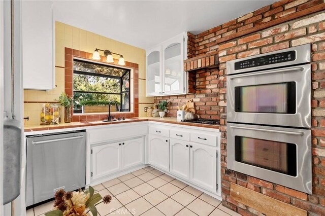 kitchen with sink, light tile patterned floors, appliances with stainless steel finishes, white cabinets, and decorative backsplash