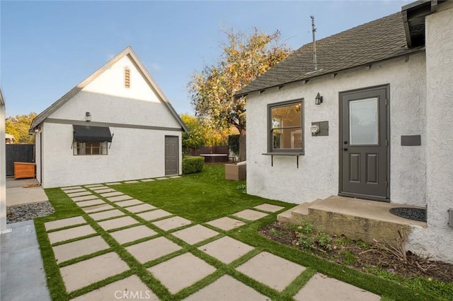 exterior space with a yard, a shingled roof, fence, and stucco siding