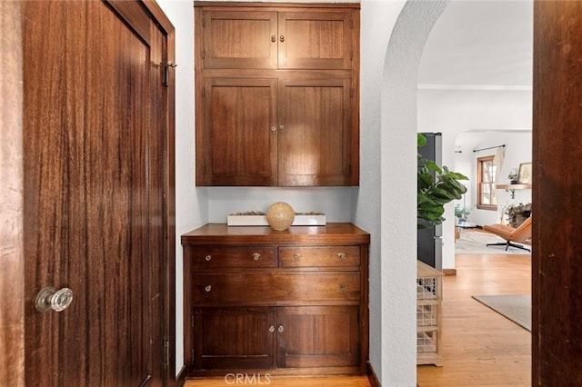 corridor featuring arched walkways, crown molding, and light wood-style floors