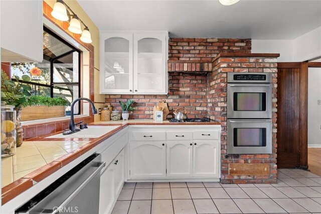 kitchen with sink, light tile patterned floors, appliances with stainless steel finishes, white cabinetry, and tile countertops