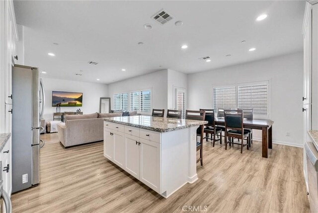 kitchen featuring stainless steel refrigerator, white cabinetry, light stone countertops, a kitchen island, and light wood-type flooring