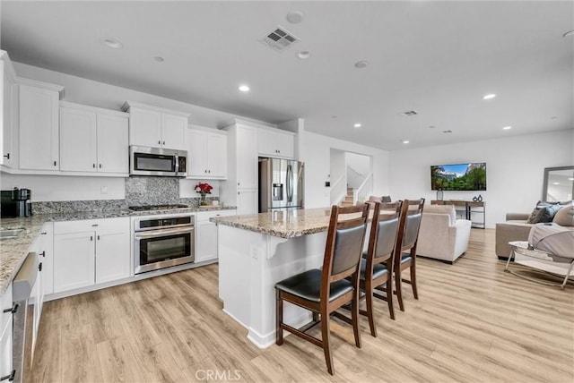 kitchen featuring white cabinetry, a breakfast bar, stainless steel appliances, and light stone countertops