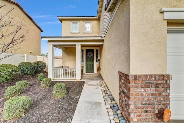 property entrance featuring a garage, covered porch, fence, and stucco siding