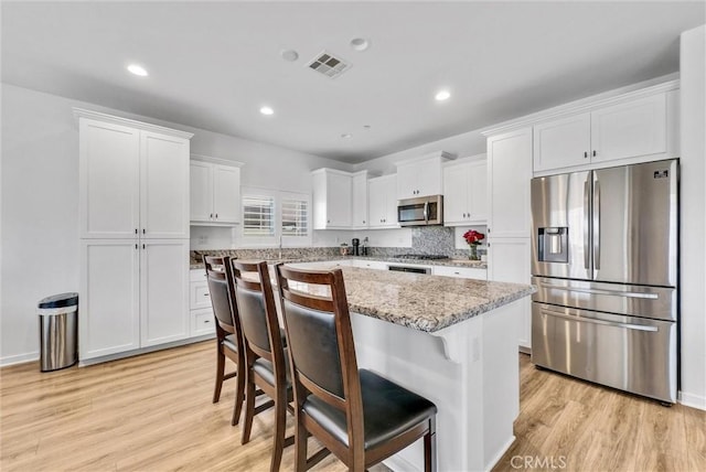 kitchen featuring stainless steel appliances, white cabinetry, a center island, and a breakfast bar