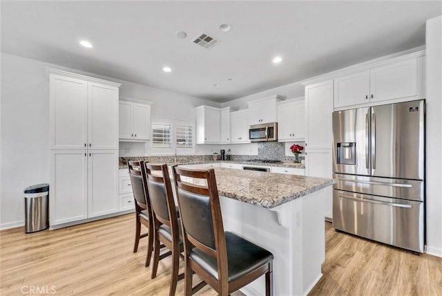 kitchen featuring visible vents, white cabinets, a breakfast bar area, stainless steel appliances, and light wood-type flooring