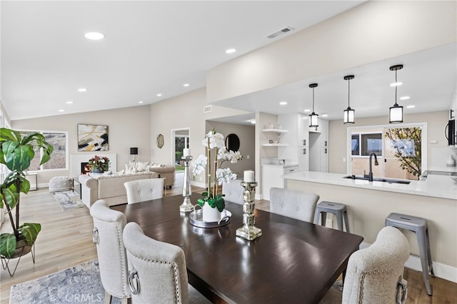 dining space with vaulted ceiling, sink, and light hardwood / wood-style flooring