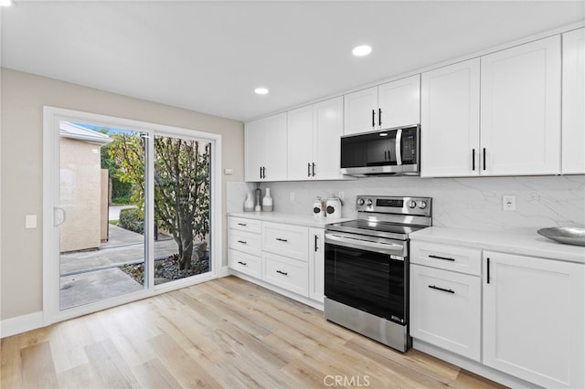 kitchen with stainless steel appliances, white cabinetry, backsplash, and light wood-type flooring