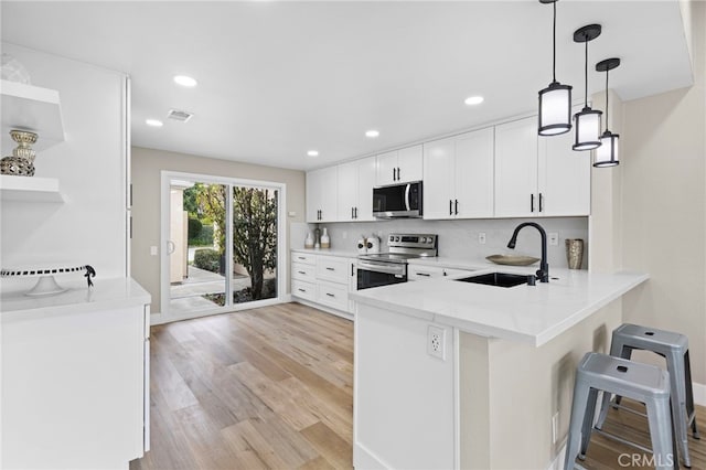 kitchen with pendant lighting, sink, white cabinets, kitchen peninsula, and stainless steel appliances