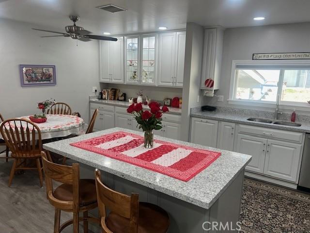 kitchen with a center island, visible vents, white cabinetry, a sink, and a kitchen bar