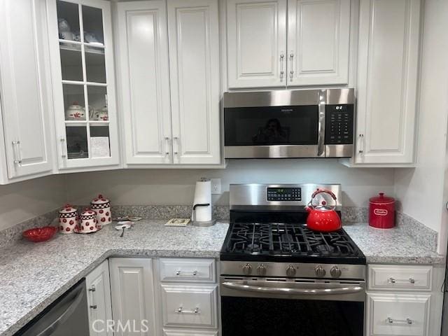 kitchen featuring appliances with stainless steel finishes, glass insert cabinets, and white cabinets