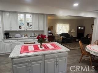 kitchen featuring white cabinets, a kitchen island, open floor plan, and wood finished floors