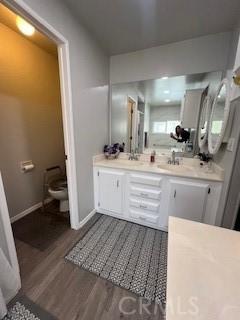 bathroom with double vanity, toilet, a sink, wood finished floors, and baseboards