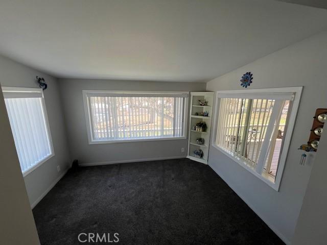 spare room with baseboards, dark carpet, and vaulted ceiling