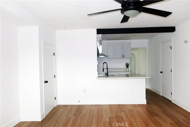 kitchen featuring wood-type flooring, sink, gray cabinetry, ceiling fan, and wall chimney range hood