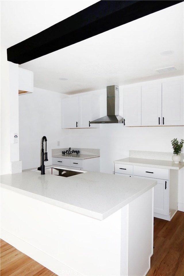 kitchen with dark hardwood / wood-style floors, white cabinetry, sink, kitchen peninsula, and wall chimney exhaust hood