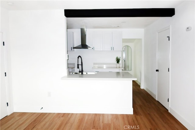 kitchen featuring sink, hardwood / wood-style flooring, wall chimney exhaust hood, white cabinets, and beamed ceiling