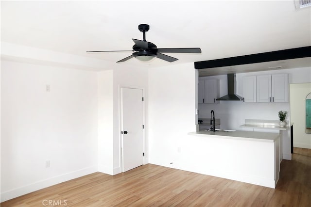 kitchen featuring wall chimney range hood, sink, ceiling fan, gray cabinetry, and hardwood / wood-style floors