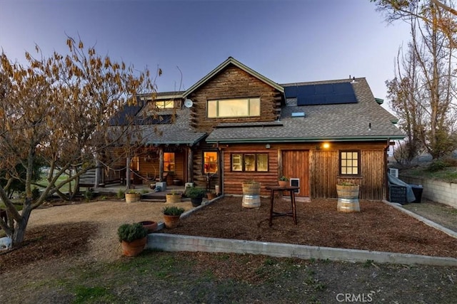 back of house at dusk featuring solar panels and roof with shingles