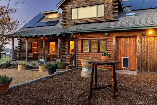 rear view of house featuring a patio, roof mounted solar panels, log exterior, and roof with shingles