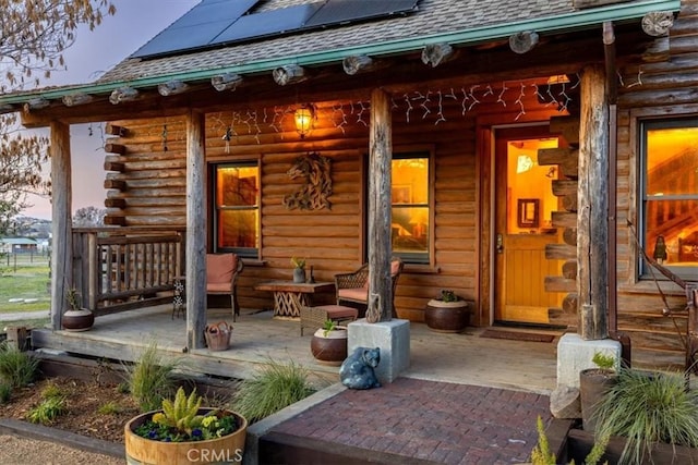 property entrance featuring covered porch, solar panels, log exterior, and roof with shingles