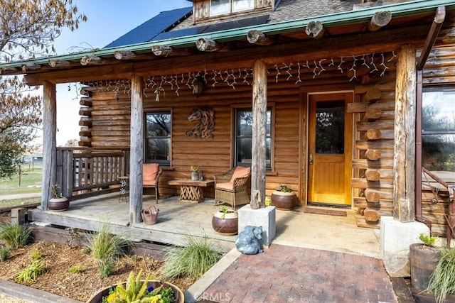 view of exterior entry featuring covered porch, log exterior, and a shingled roof