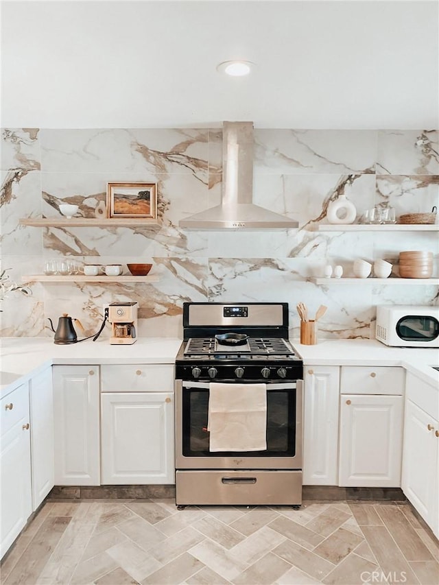 kitchen with stainless steel gas range oven, ventilation hood, tasteful backsplash, and white cabinets