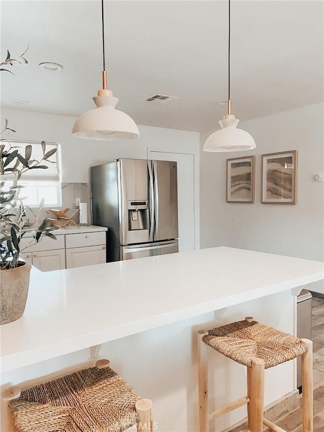 kitchen with decorative light fixtures, a breakfast bar area, white cabinets, and stainless steel fridge with ice dispenser