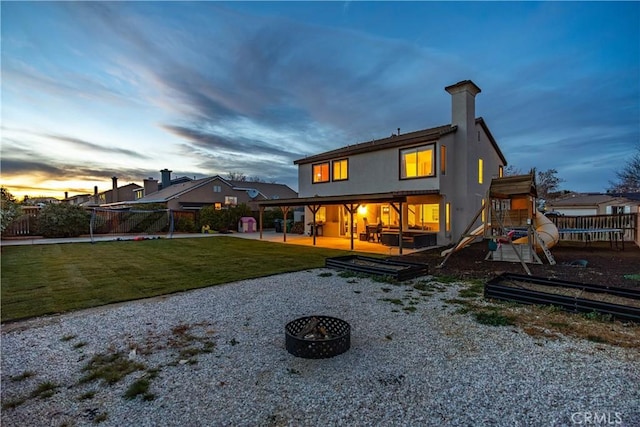 back house at dusk featuring an outdoor fire pit, a yard, a playground, and a patio area