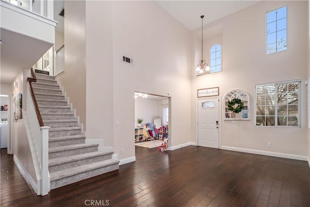 entryway with dark wood-type flooring, a towering ceiling, and a notable chandelier