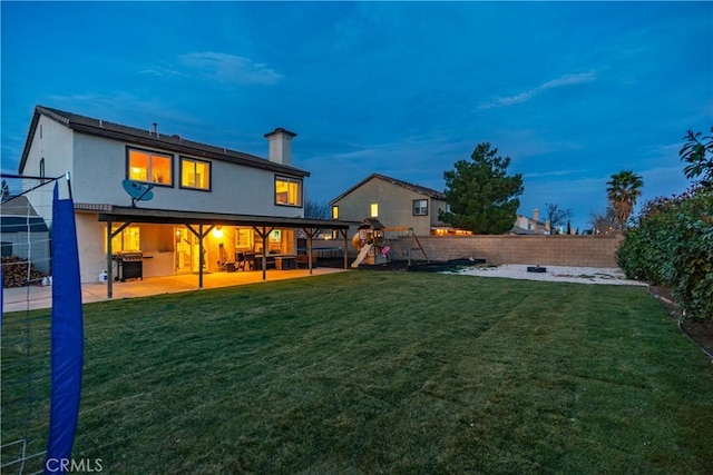 back house at dusk with a playground, a patio, and a lawn