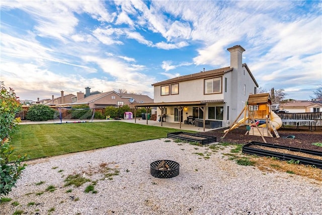 rear view of property featuring a patio, a yard, a playground, and a fire pit