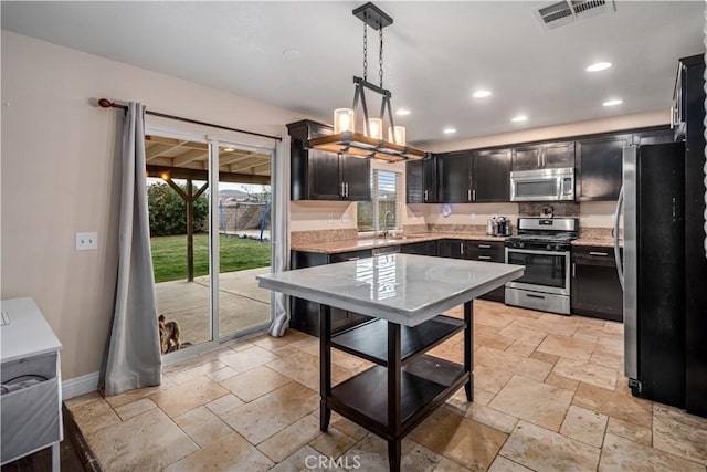 kitchen featuring pendant lighting, stainless steel appliances, sink, and light stone counters