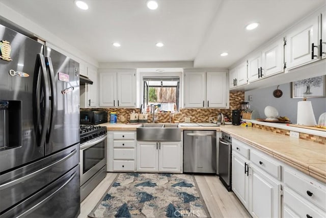 kitchen featuring sink, light hardwood / wood-style flooring, white cabinetry, stainless steel appliances, and tasteful backsplash