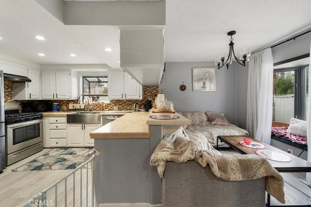 kitchen with stainless steel gas stove, hanging light fixtures, tasteful backsplash, and white cabinets